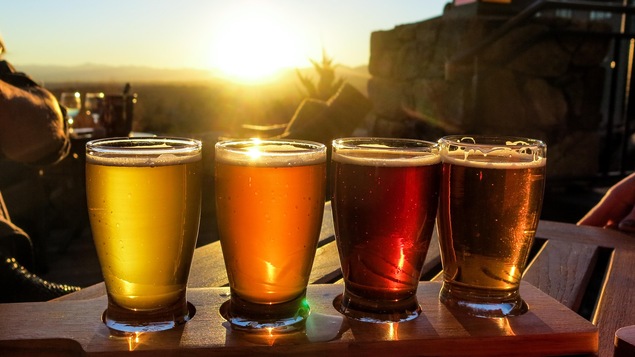 Quatre verres de bière en palette de dégustation sur fond de coucher de soleil.