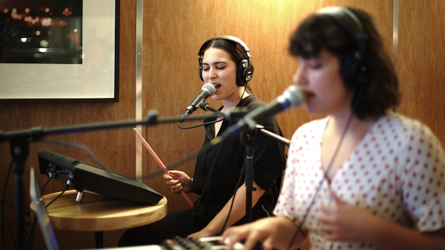 Camille Poliquin, une baguette à la main, et Laurence Lafond-Beaulne, une main sur un clavier, chantent dans un micro.