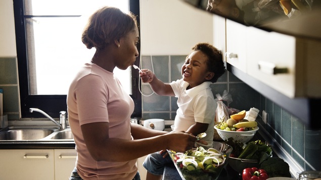 Une femme cuisine en compagnie de son enfant.