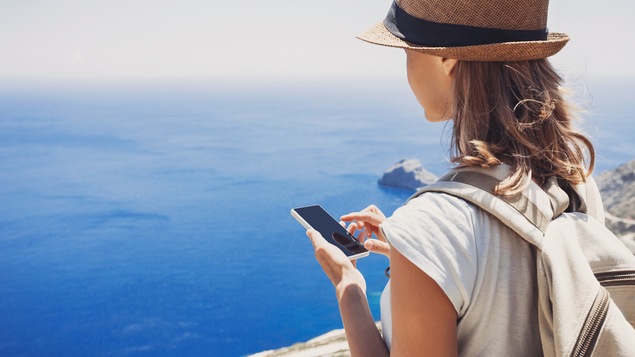 Une voyageuse consulte son téléphone intelligent devant une vue imprenable.