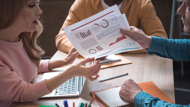 Une femme commente des statistiques avec des collègues de travail.