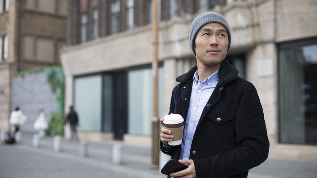 Un jeune homme marche dans la rue avec un café pour emporter dans la main.