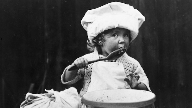 Une petite cuisinière teste la qualité des ingrédients en léchant une cuillère, sur cette photo datant de 1935.