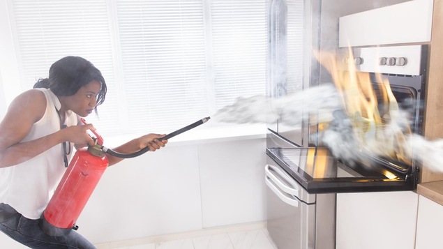 Une femme utilise un extincteur pour contenir un feu de cuisson.