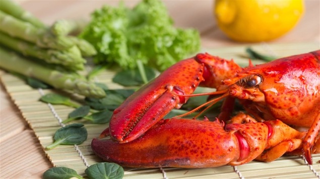 Un homard cuit est posé sur un naperon avec des asperges, des herbes et un citron.