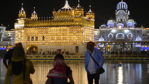 Trois touristes sont devant le Temple d'or, à Amritsar en Inde, le soir.
