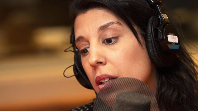 Une femme est devant un micro, la tête légèrement de côté.