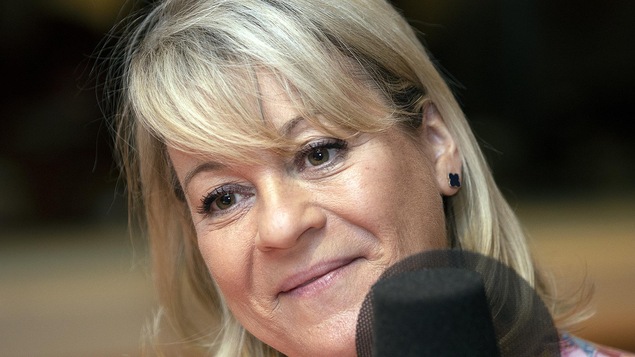 Une femme, la tête légèrement penchée, est devant un micro.