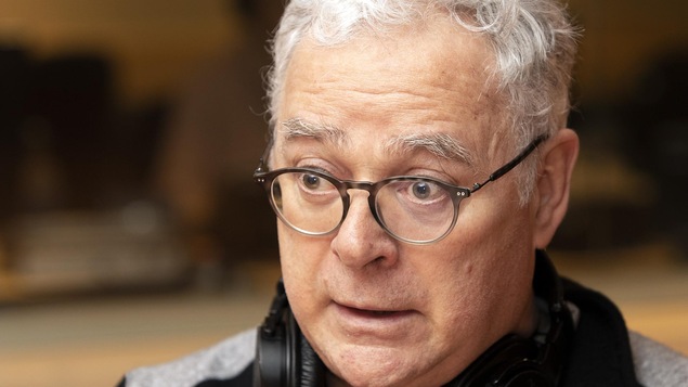 Un homme portant des lunettes parle devant un micro.