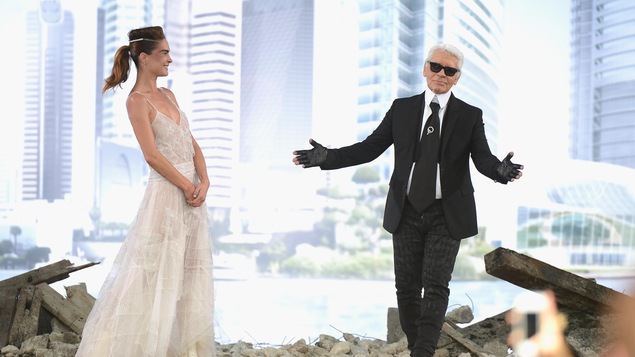 Karl Lagerfeld fait un salut sur scène, à côté d'un mannequin qui lui sourit.