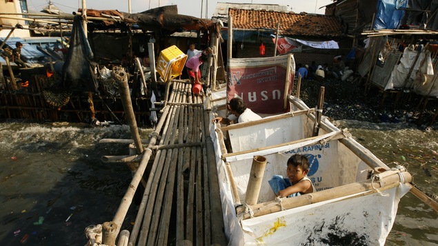 Un adulte et un enfant utilisent des latrines publiques se jetant dans la mer dans un bidonville de Jakarta, en Indonésie.