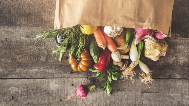 Des légumes frais sortant d'un sac de papier renversé sur une table.