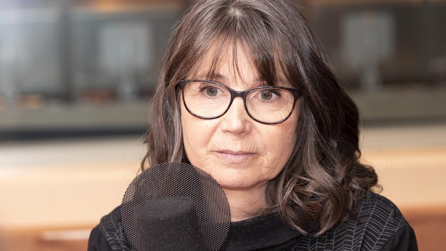 Une femme portant des lunettes est devant un micro.