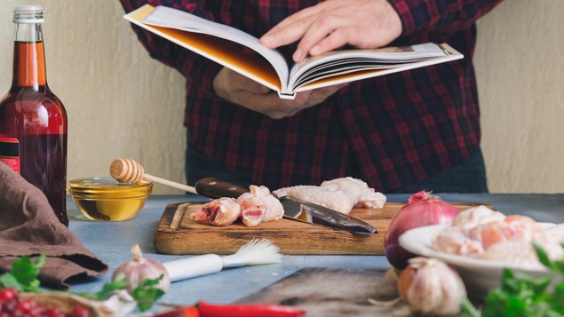 Un homme tient un livre de recettes au-dessus d'un comptoir de cuisine plein d'ingrédients.