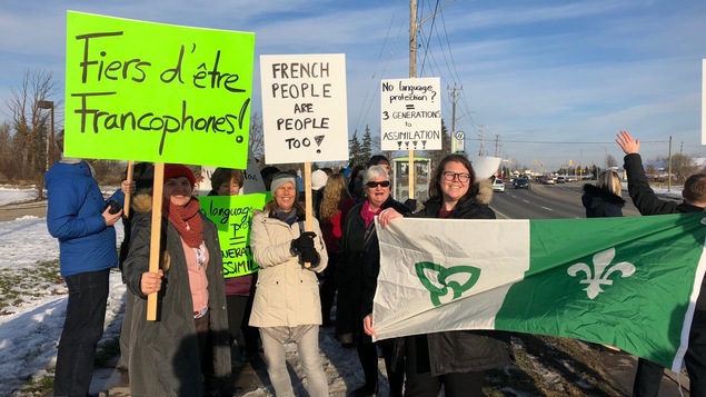 Des manifestants avec des enseignes et un drapeau franco-ontarien à Cambridge, en Ontario.