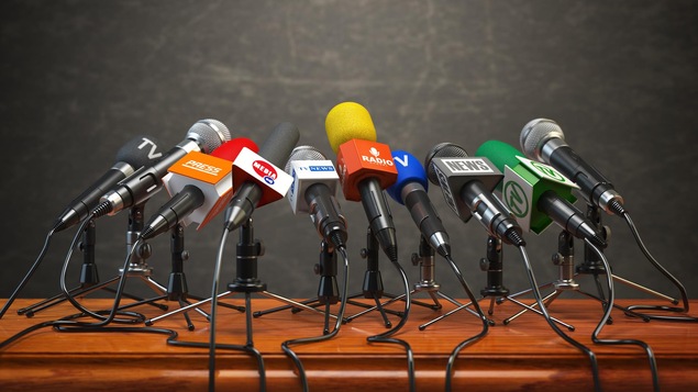 Des microphones de différents médias disposés sur un podium.