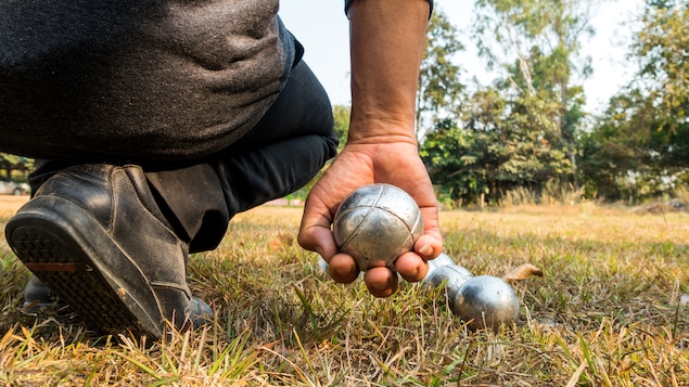 Un homme accroupi tient une boule de pétanque.