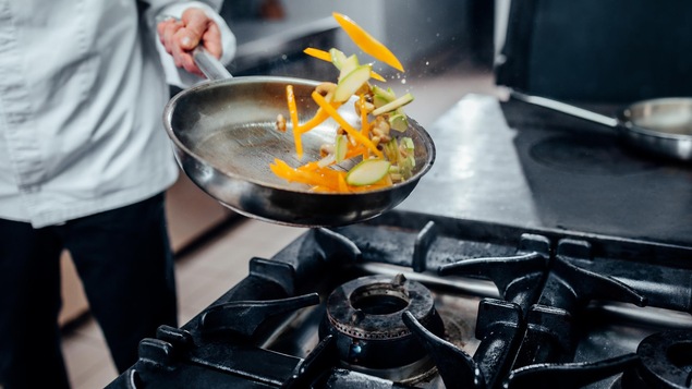 Un cuisiner fait sauter des légumes dans une poêle.