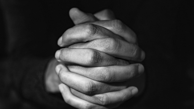 Photo en noir et blanc, en gros plan, des mains d'un homme en train de prier.