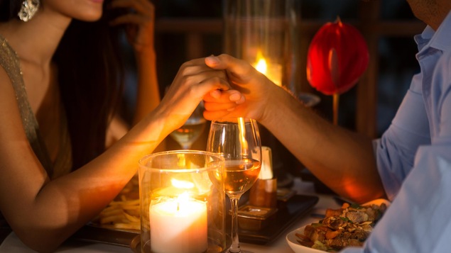 Un couple partage un repas romantique autour de bougies et d'une rose.