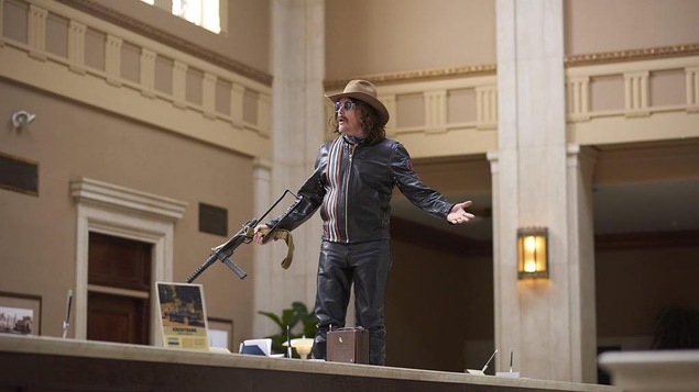 Un homme habillé de cuir, un chapeau de cowboy et tenant une mitraillette est debout sur le comptoir d'une banque.