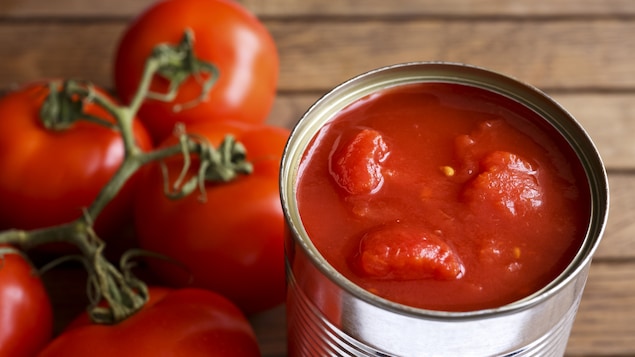 Des tomates fraîches à côté d'une conserve de tomates ouverte