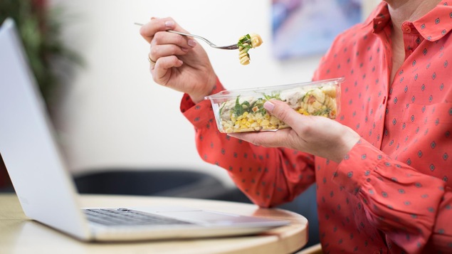 Une femme mange son lunch à son bureau au travail.