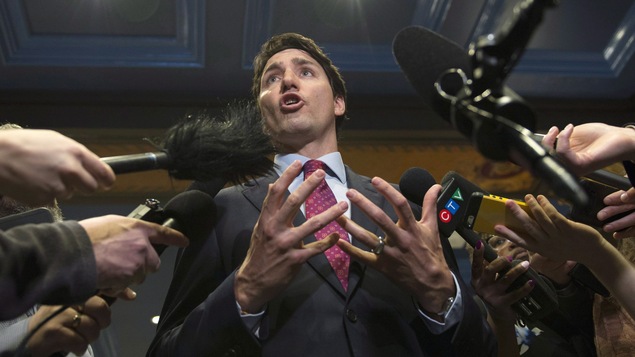 Le premier ministre Trudeau entouré de journalistes qui lui tendent leur micro.