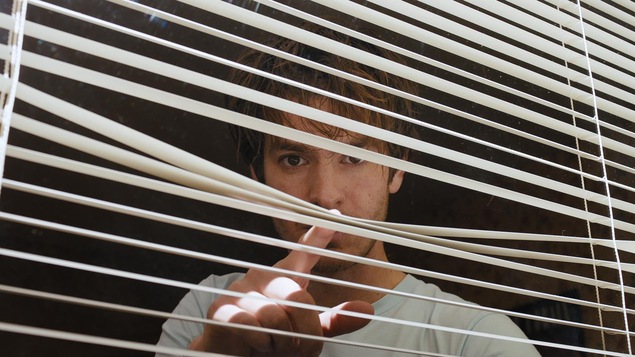 Andrew Garfield regarde à travers les stores d'une fenêtre dans cette image tirée du film <i>Under the Silver Lake</i>, de David Robert Michell.
