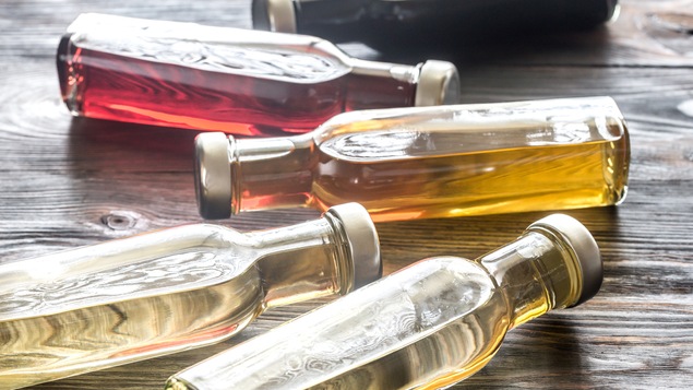Quatre bouteilles contenant différents vinaigres reposent à l'horizontal sur une table.