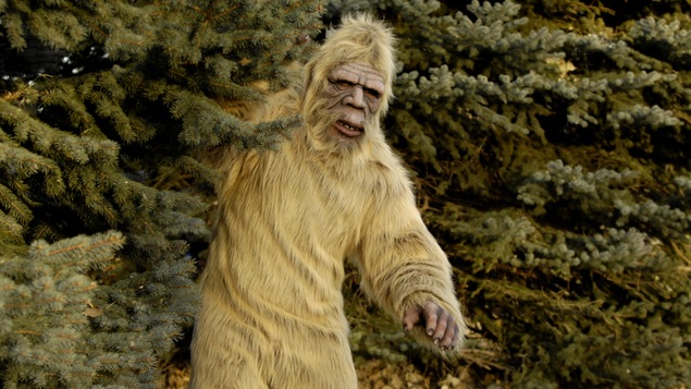 Un homme costumé en yéti, en sasquatch ou en abominable homme des neiges, partiellement dissimulé derrière un arbre