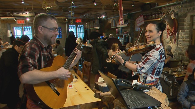 Un homme joue de la guitare et une femme joue du violon dans un restaurant, devant les clients.