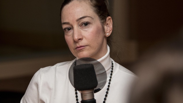 Elle porte un col-roulé blanc et un long collier noir.