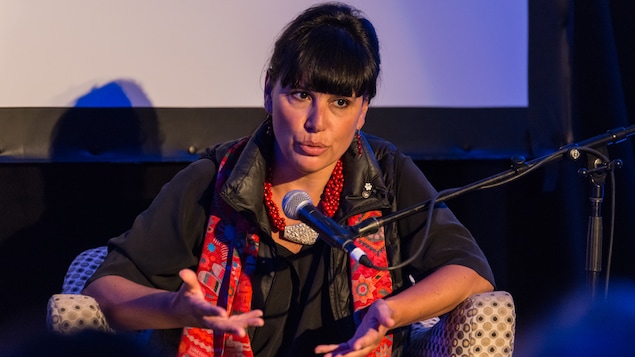 Nathalie Bondil parle dans un micro sur une scène, assise dans un fauteuil