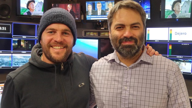Les deux amis sont debout devant plusieurs écrans de télévision.