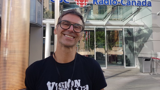 Un homme est appuyé contre une colonne à l'avant de l'édifice de Radio-Canada.