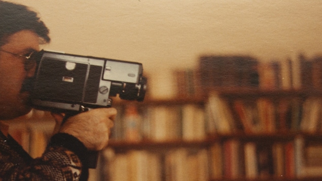 Joseph Morder filme avec une caméra Super 8 devant une bibliothèque.