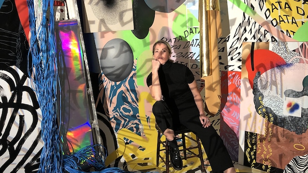 Cyndie Belhumeur pose devant une installation de collages colorés et de fils réseaux.