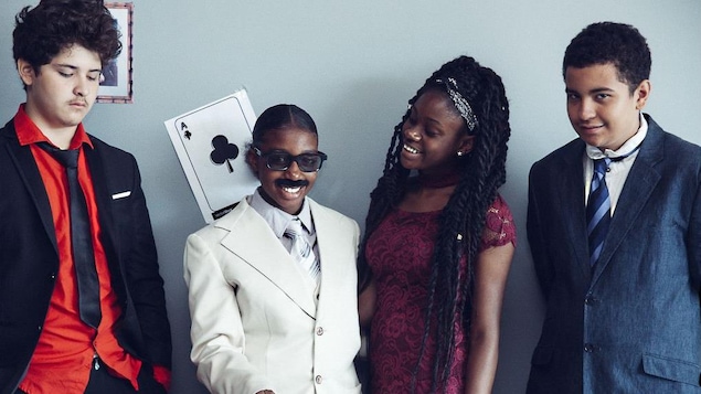 Quatre adolescents habillés de complets posent pour le photographe, souriants.