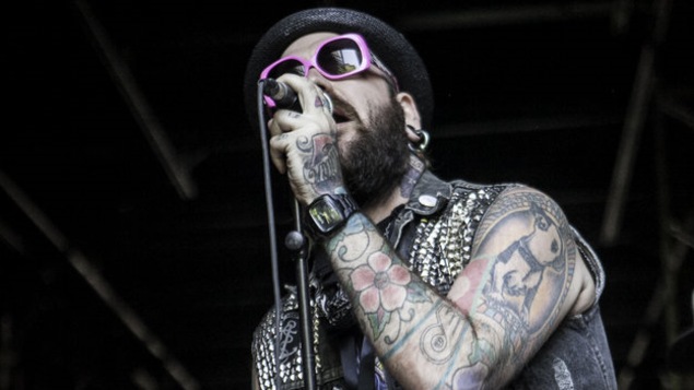 Un chanteur aux nombreux tatouages porte des lunettes roses sur scène.