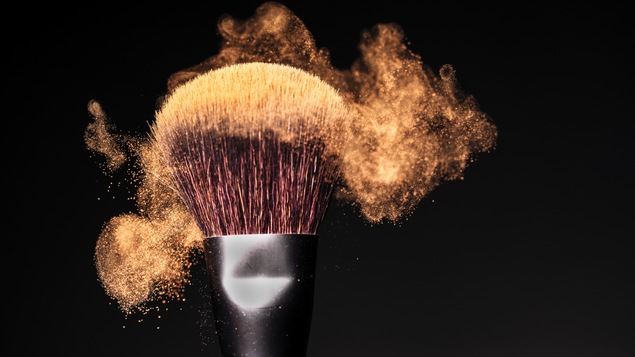 Un pinceau à maquillage avec de la poudre brillante, sur fond noir.