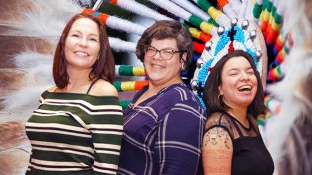 Portrait des trois femmes avec un motif de perlage et de plumes en arrière-plan.