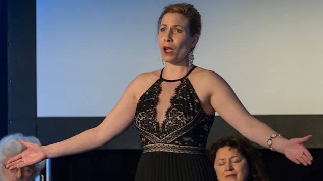 La mezzo-soprano Caroline Gélinas chante sur une scène dans une robe de bal noire.