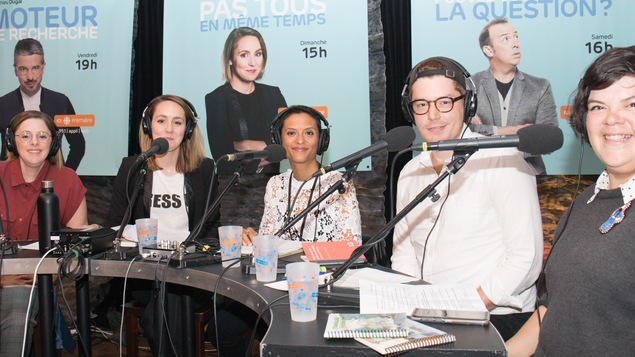 Les cinq personnes sont autour d'un table avec des écouteurs sur les oreilles et regardent la caméra.