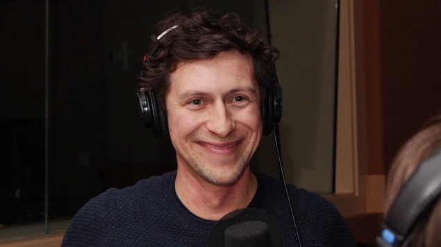Un homme est devant un micro où il répond à des questions dans un studio de radio.