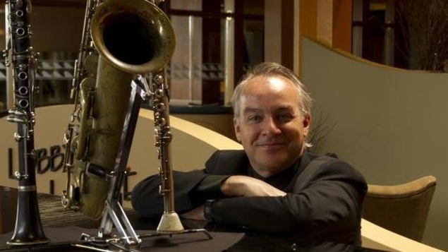 Paul Lamoureux sourit assis à côté d'un saxophone mis sur une table.