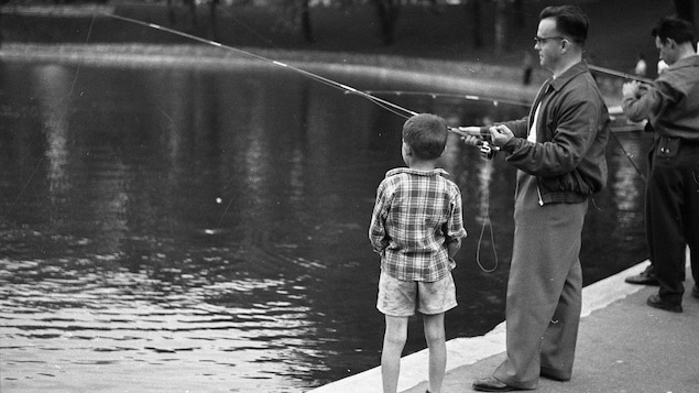 Photo en noir et blanc montrant un homme et un enfant en train de pêcher au bord d'un bassin.