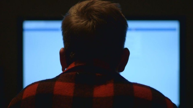 Photo d'un homme de dos qui regarde un écran d'ordinateur.