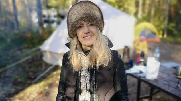 Photo d'Evelyne Charuest, habillée en vêtements d'extérieur, avec des bottes et un chapeau de fourrure, qui pose devant une tente de camping.