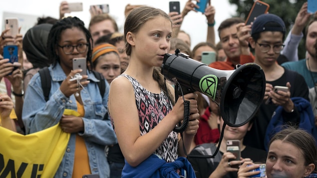 Photo de Greta Thunberg qui parle dans un porte-voix devant une foule de jeunes gens.